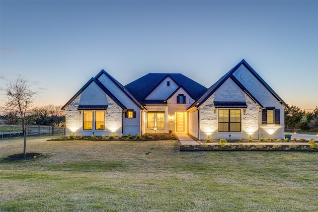 french country style house with a yard, fence, and brick siding