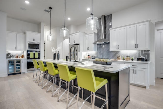 kitchen with a kitchen breakfast bar, wall chimney range hood, a sink, beverage cooler, and stainless steel appliances
