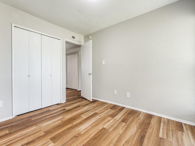 unfurnished bedroom featuring light wood-style floors, baseboards, and a closet