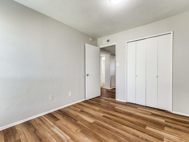 unfurnished bedroom featuring wood finished floors, baseboards, a closet, and a textured ceiling