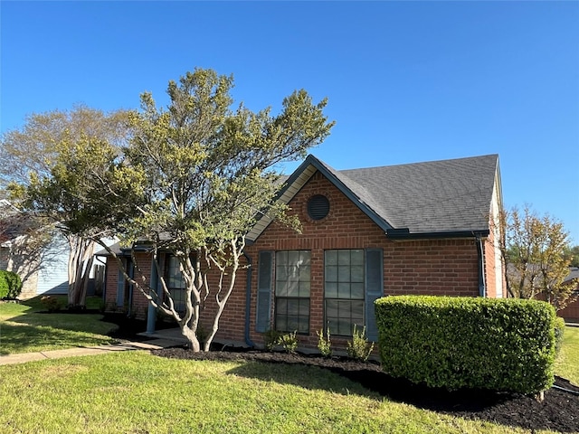 view of front of house featuring brick siding, a shingled roof, and a front yard