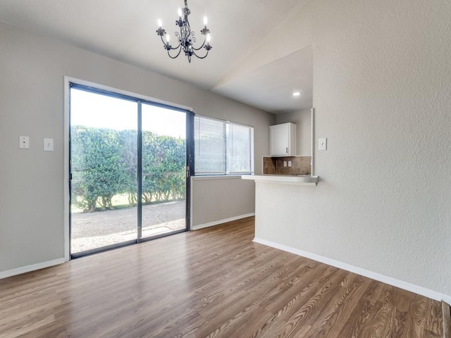 unfurnished living room with a chandelier, wood finished floors, lofted ceiling, baseboards, and a textured wall