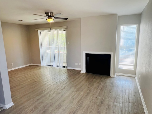 unfurnished living room featuring plenty of natural light, a ceiling fan, wood finished floors, and baseboards