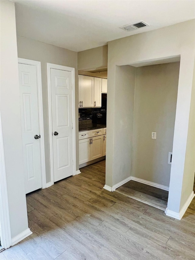 kitchen featuring dark countertops, wood finished floors, baseboards, white cabinetry, and visible vents