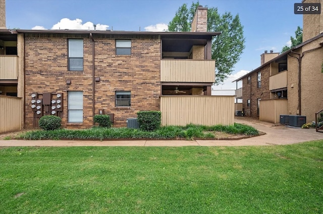 rear view of property with a chimney, cooling unit, and a lawn