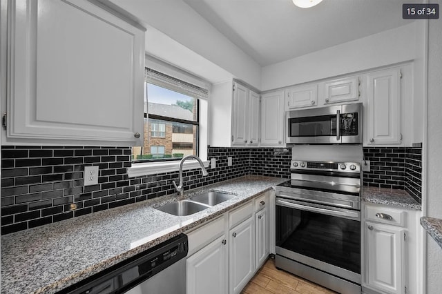 kitchen featuring white cabinets, stainless steel appliances, backsplash, a sink, and light wood-style floors