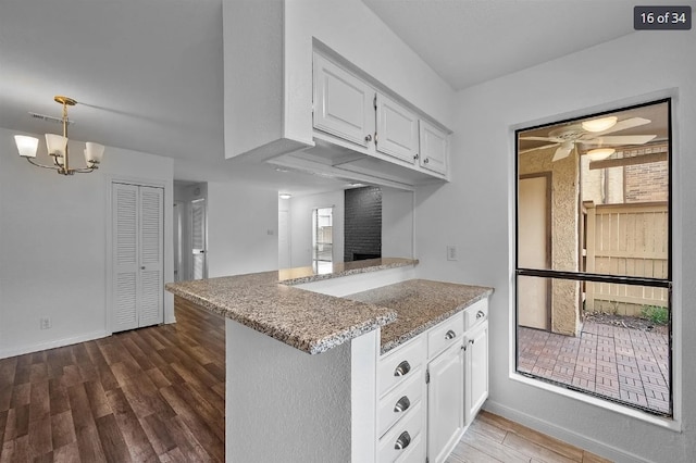 kitchen with white cabinets, a peninsula, dark wood finished floors, ceiling fan with notable chandelier, and light stone countertops
