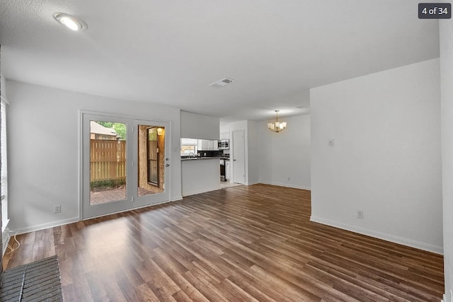 unfurnished living room featuring baseboards, dark wood-type flooring, visible vents, and a notable chandelier