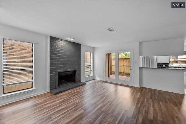 unfurnished living room with a sink, dark wood finished floors, baseboards, visible vents, and a fireplace