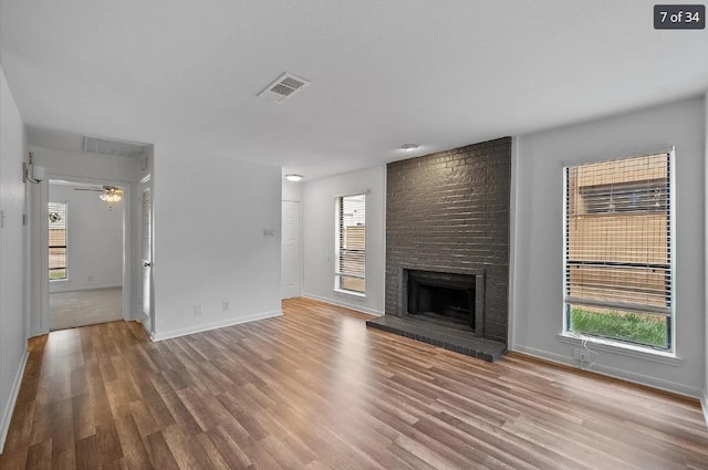 unfurnished living room featuring wood finished floors, visible vents, a wealth of natural light, and a brick fireplace