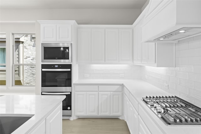 kitchen featuring custom exhaust hood, white cabinets, decorative backsplash, and stainless steel appliances