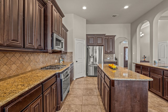 1109 Mount Ln, Rhome, TX 76078 - kitchen with appliances with stainless steel finishes, arched walkways, a kitchen island, light stone countertops, and dark brown cabinets