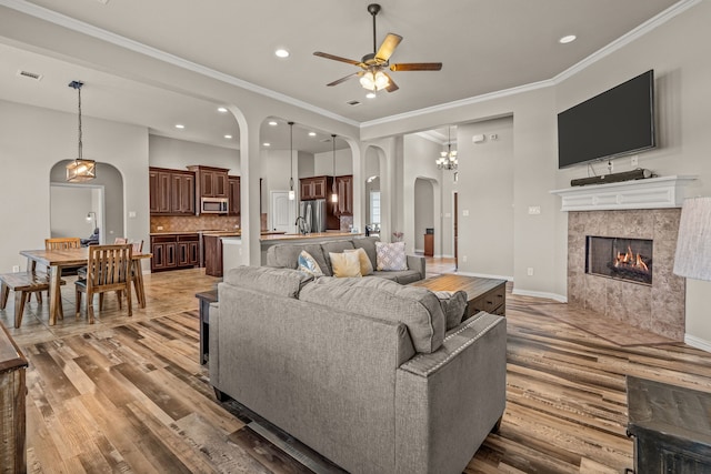 1109 Mount Ln, Rhome, TX 76078 - living area featuring arched walkways, light wood-style flooring, ceiling fan, a tiled fireplace, and ornamental molding