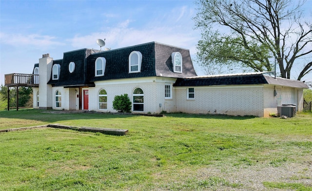 back of property with brick siding, roof with shingles, a lawn, and mansard roof