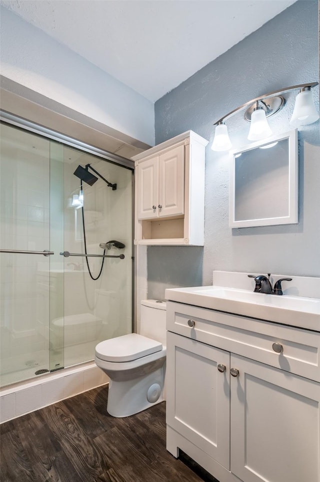 bathroom with toilet, vanity, a shower stall, and wood finished floors