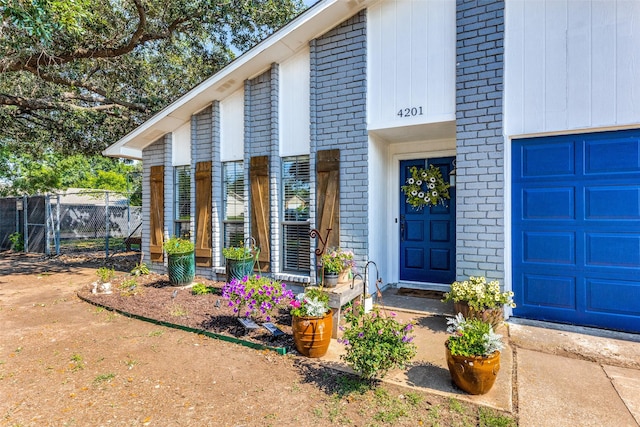 entrance to property featuring fence, brick siding, and a garage