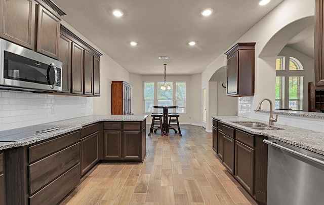 kitchen with arched walkways, dark brown cabinetry, a sink, and appliances with stainless steel finishes