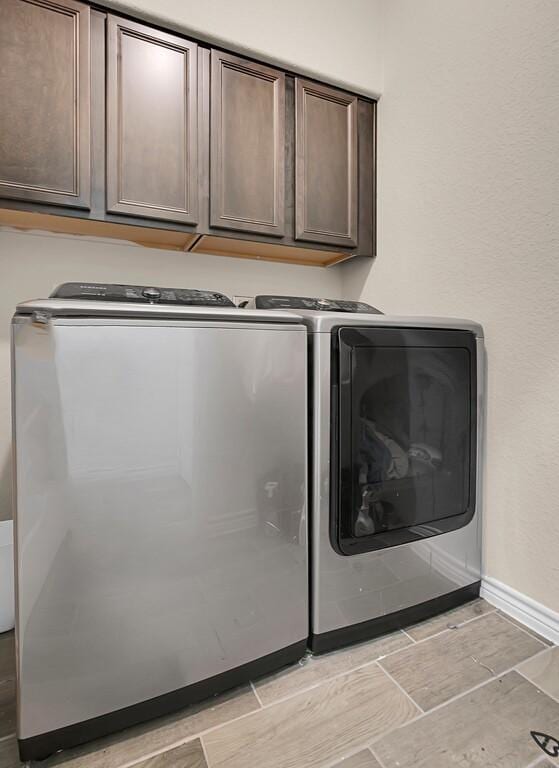 clothes washing area featuring wood tiled floor, washing machine and clothes dryer, baseboards, and cabinet space
