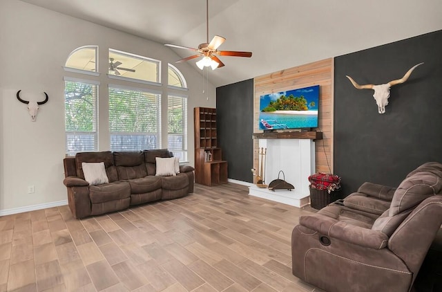 living room with light wood-style floors, ceiling fan, high vaulted ceiling, an accent wall, and baseboards