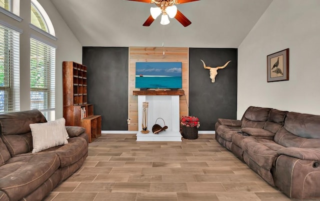 living area featuring baseboards, an accent wall, ceiling fan, wood finish floors, and high vaulted ceiling