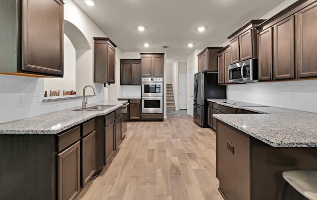 kitchen featuring appliances with stainless steel finishes, a sink, light stone counters, and dark brown cabinets
