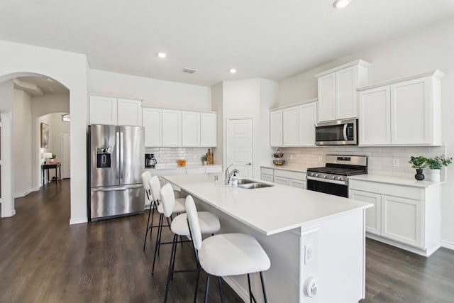 13412 Cortes De Pallas Dr, Little Elm, TX 75068 - kitchen featuring stainless steel appliances, a sink, a center island with sink, dark wood finished floors, and arched walkways