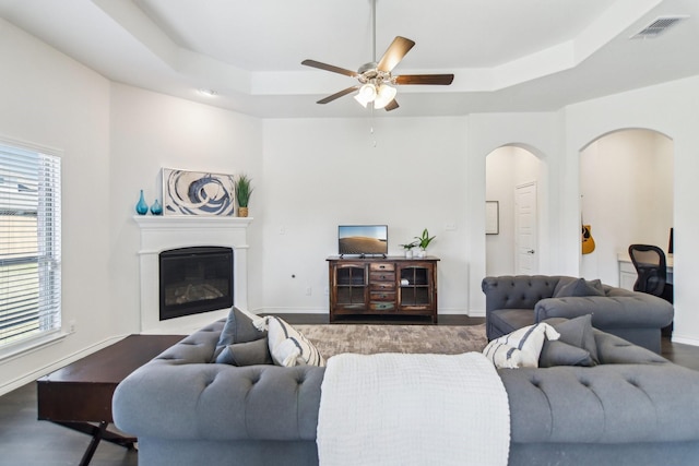 13412 Cortes De Pallas Dr, Little Elm, TX 75068 - living area featuring a tray ceiling, ceiling fan, arched walkways, a glass covered fireplace, and baseboards