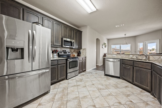 kitchen with dark brown cabinetry, tasteful backsplash, arched walkways, appliances with stainless steel finishes, and a sink