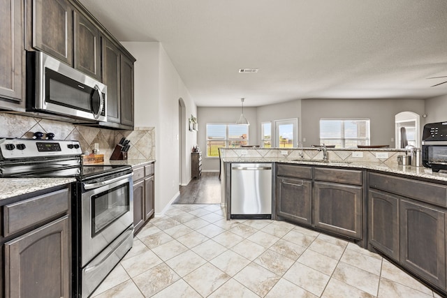 kitchen featuring tasteful backsplash, arched walkways, dark brown cabinets, a sink, and stainless steel appliances
