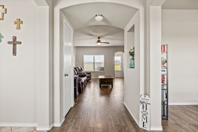 hall featuring baseboards, arched walkways, and wood finished floors