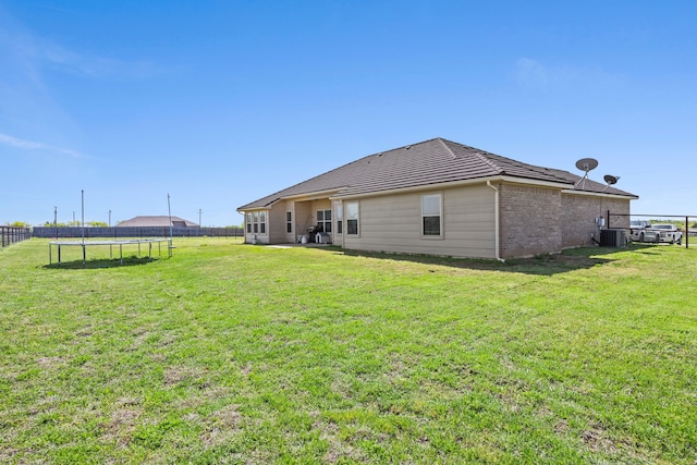 back of house featuring cooling unit, a yard, fence, brick siding, and a trampoline