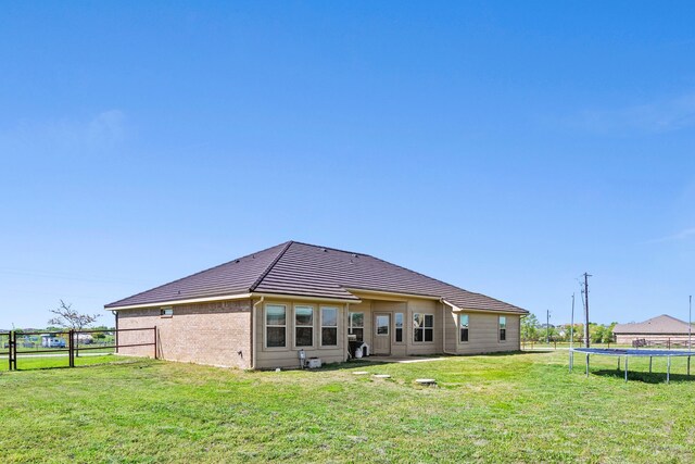 rear view of property featuring a tiled roof, a trampoline, a lawn, fence, and brick siding
