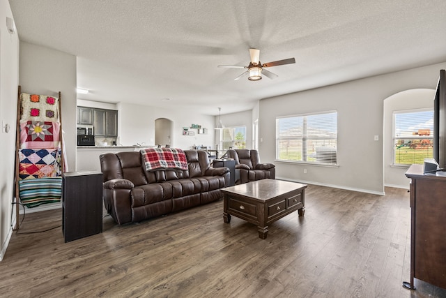 living room with dark wood-style flooring, a ceiling fan, arched walkways, and a textured ceiling