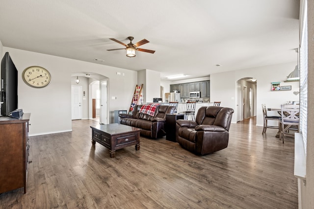 living area featuring arched walkways, baseboards, a ceiling fan, and wood finished floors