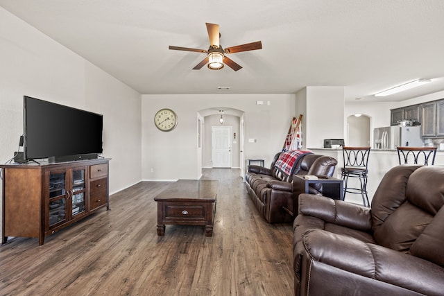 living area featuring baseboards, a ceiling fan, arched walkways, and dark wood finished floors