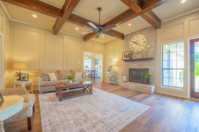 living area with a decorative wall, ceiling fan, beamed ceiling, wood finished floors, and coffered ceiling