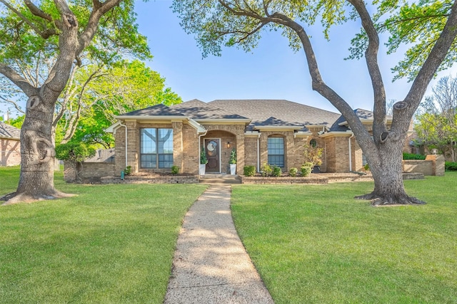view of front of property featuring roof with shingles, a front lawn, and brick siding