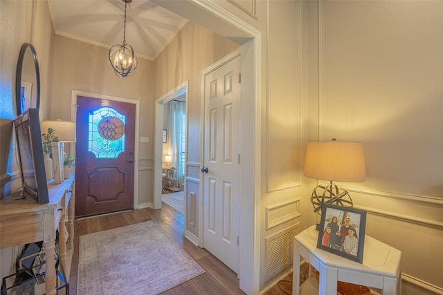 foyer entrance featuring crown molding, wood finished floors, a notable chandelier, and visible vents