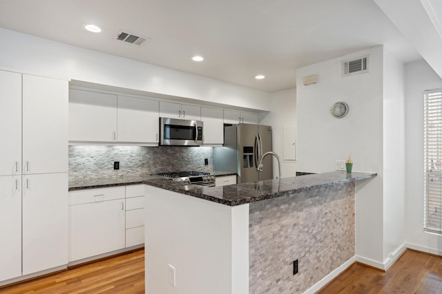 4122 Travis St Unit 7, Dallas, TX 75204 - kitchen featuring stainless steel appliances, light wood-type flooring, dark stone countertops, tasteful backsplash, and white cabinets