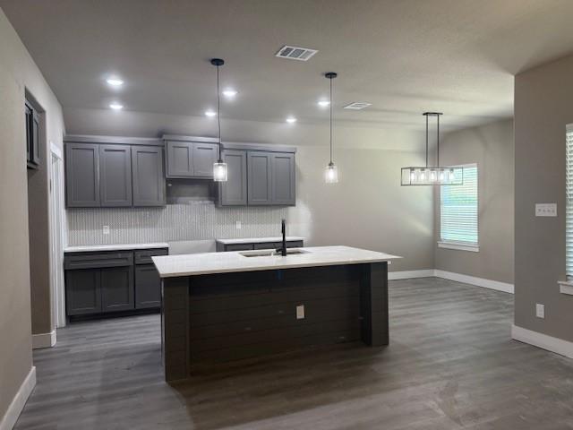 kitchen with baseboards, dark wood-style floors, visible vents, decorative backsplash, and a sink
