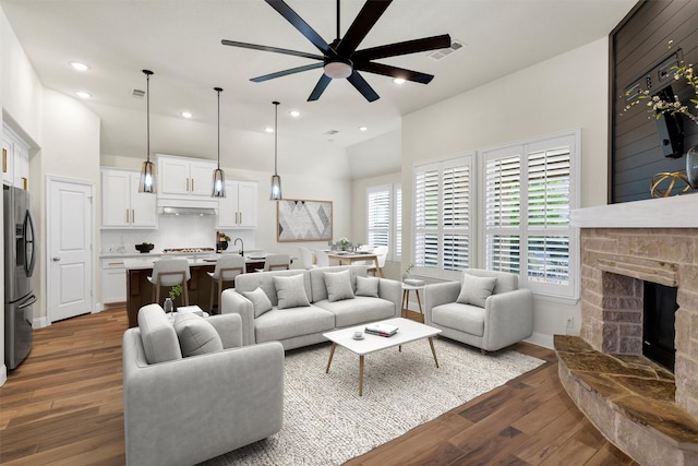 living room with a ceiling fan, a stone fireplace, visible vents, wood finished floors, and lofted ceiling