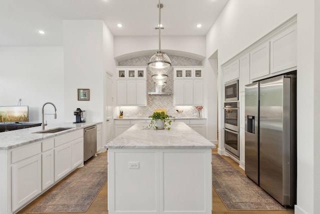 808 Bluestem Dr, Aubrey, TX 76227 - kitchen featuring stainless steel appliances, a sink, a peninsula, a kitchen island, and glass insert cabinets