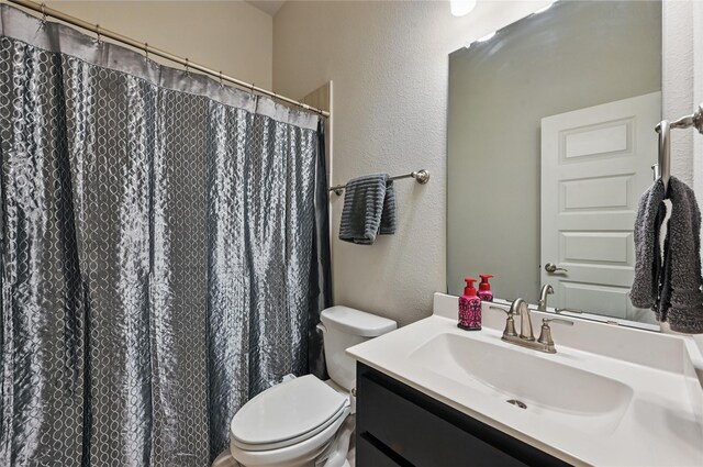 full bathroom featuring toilet, a textured wall, and vanity
