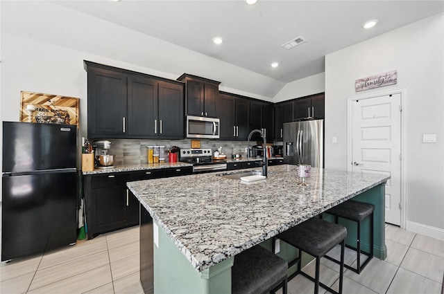 kitchen with a breakfast bar, visible vents, stainless steel appliances, light stone countertops, and backsplash