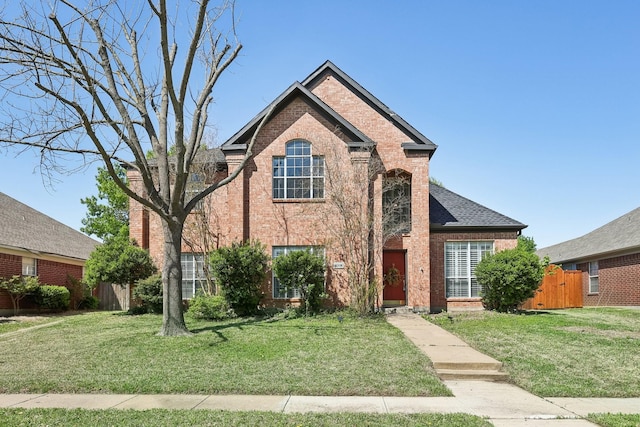 traditional home with roof with shingles, a front yard, and brick siding