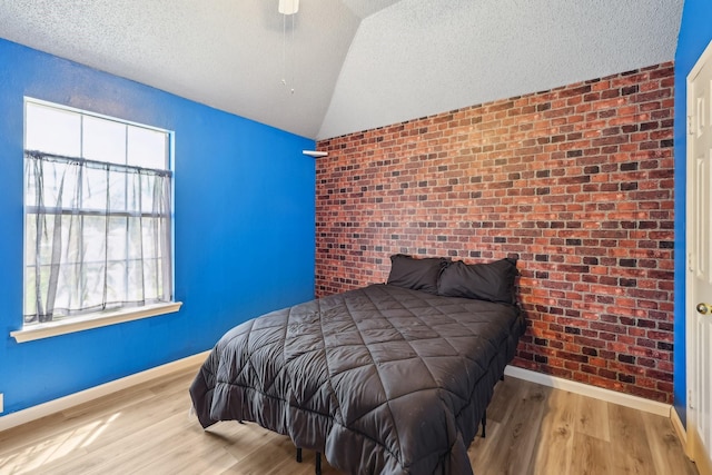 bedroom with baseboards, brick wall, a textured ceiling, lofted ceiling, and wood finished floors
