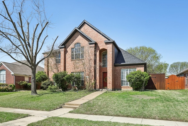 traditional home featuring a shingled roof, a gate, a front yard, and brick siding