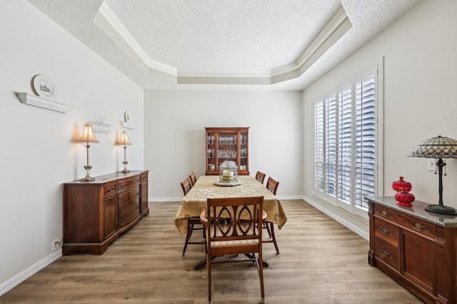 dining room with a raised ceiling, a textured ceiling, baseboards, and light wood-style flooring