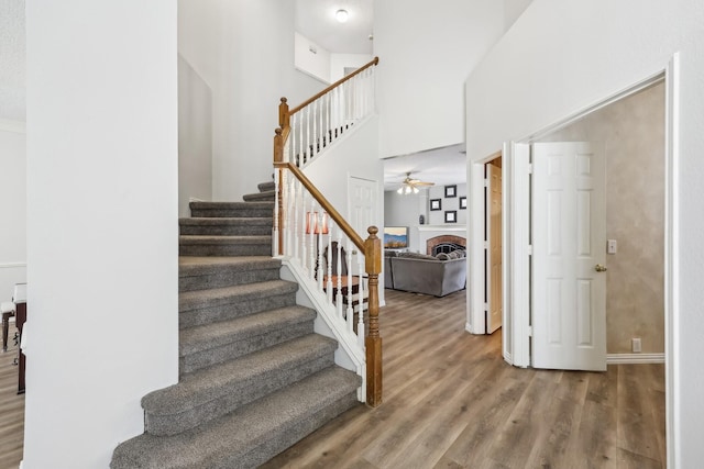 stairway with baseboards, a high ceiling, a ceiling fan, a fireplace, and wood finished floors