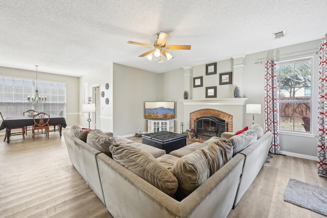 living room featuring visible vents, light wood-type flooring, a fireplace, and ceiling fan with notable chandelier